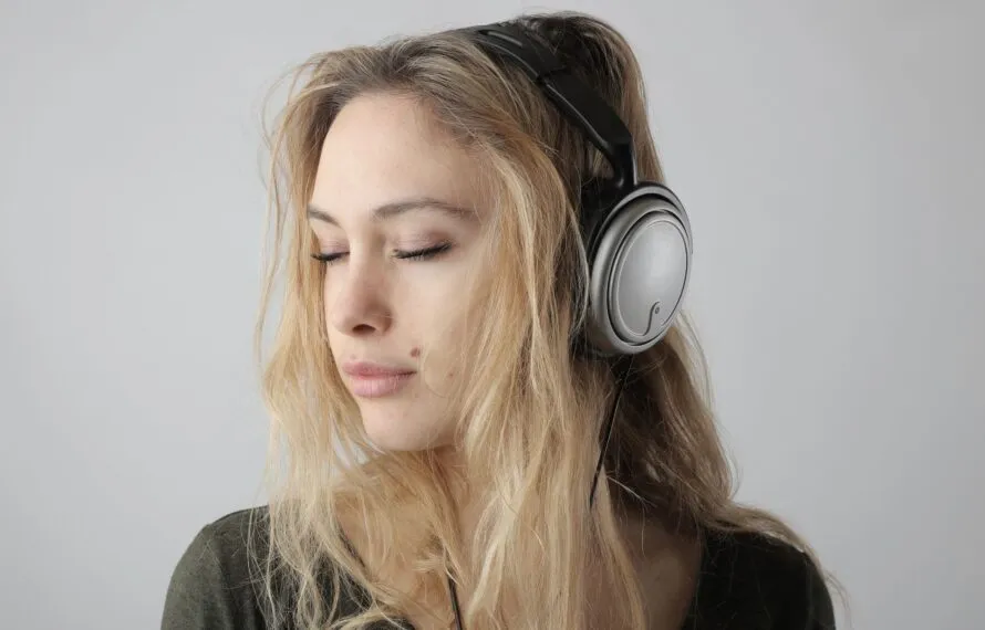 Quais são os efeitos da música no cérebro e no humor Mulher de olhos fechados ouvindo música com fones de ouvido, com expressão serena e relaxada