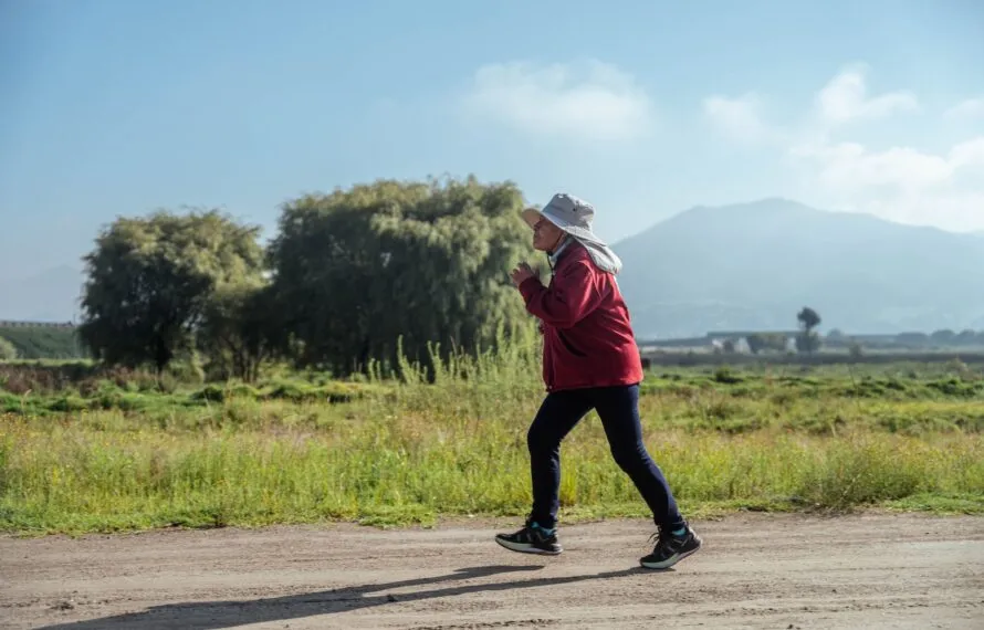 Brasileiros perdem 12,5 anos de expectativa de vida saudável para doenças e limitações Mulher em roupa esportiva caminha em ritmo acelerado por estrada de terra cercada de vegetação e montanhas