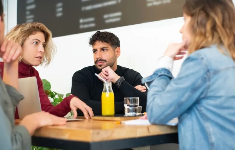 Quatro pessoas sentadas em uma mesa conversando em um café, com bebidas sobre a mesa.