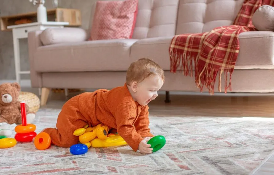 Brinquedos para bebê de 8 meses: o que observar antes de comprar Bebê em trajes laranja brincando no chão com brinquedos coloridos.